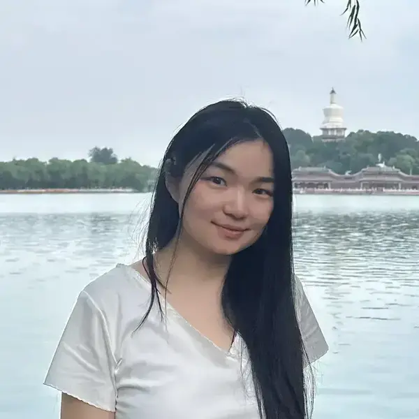 Young Asian woman in white smiles by Beihai Park lake. The White Dagoba and ornate pavilions rise on the hill.